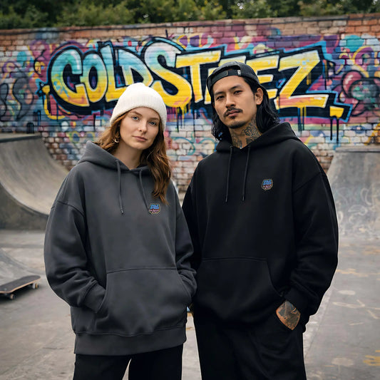 Two people wearing hoodies in front of a graffiti-covered wall at a skate park.