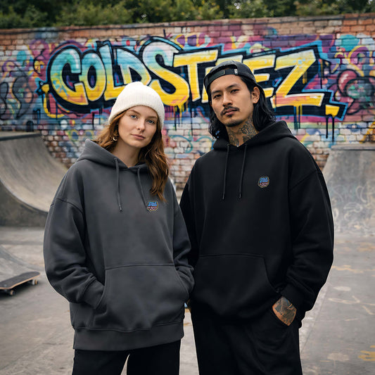 Two people wearing hoodies in front of a graffiti-covered wall at a skate park.